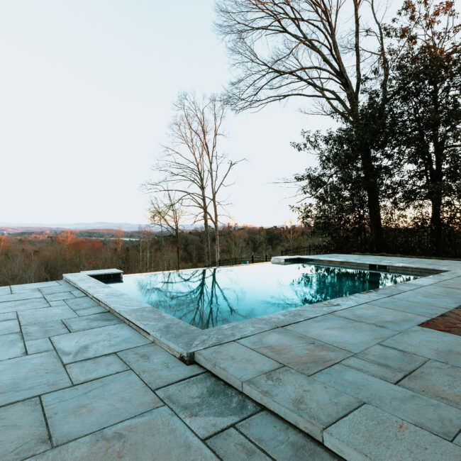 Infinity pool with flagstone deck and bare trees at dusk in Mountain Vista by Mike Stevens Homes
