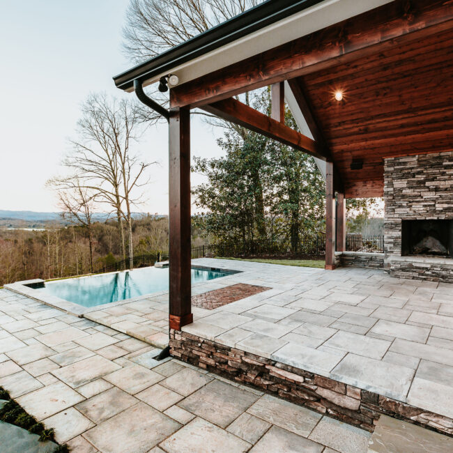 Covered stone fireplace patio with pool view and wood beamed pergola in Mountain Vista by Mike Stevens Homes