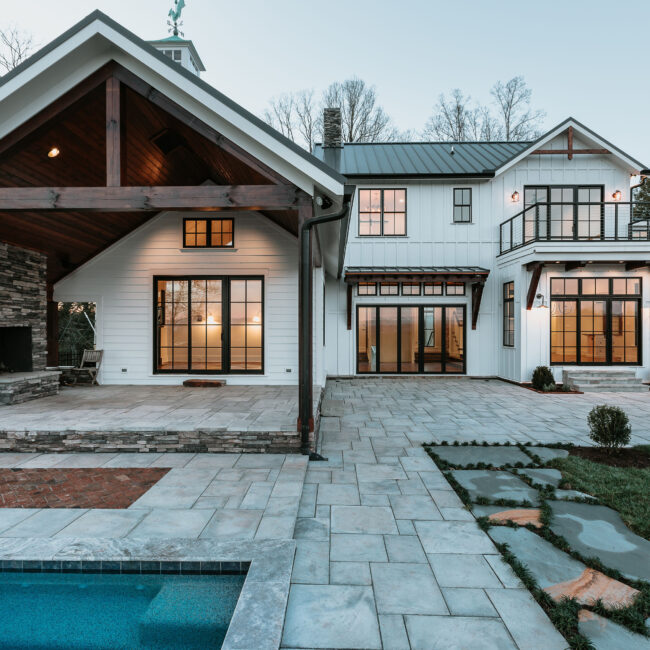 Rear of white farmhouse with stone patio, wood beams and pool in Mountain Vista by Mike Stevens Homes