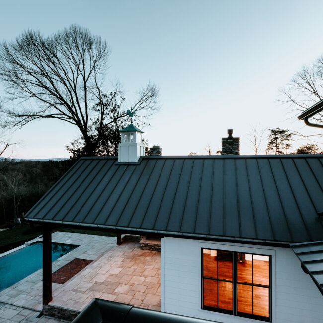 Black standing-seam metal roof over pool patio with glowing windows in Mountain Vista by Mike Stevens Homes
