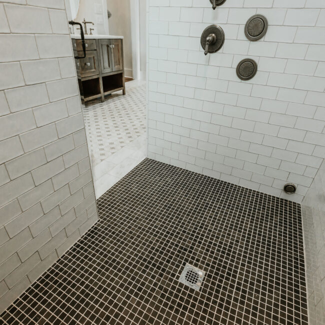 Walk-in shower with black hex floor tile and multiple shower heads in Mountain Vista by Mike Stevens Homes