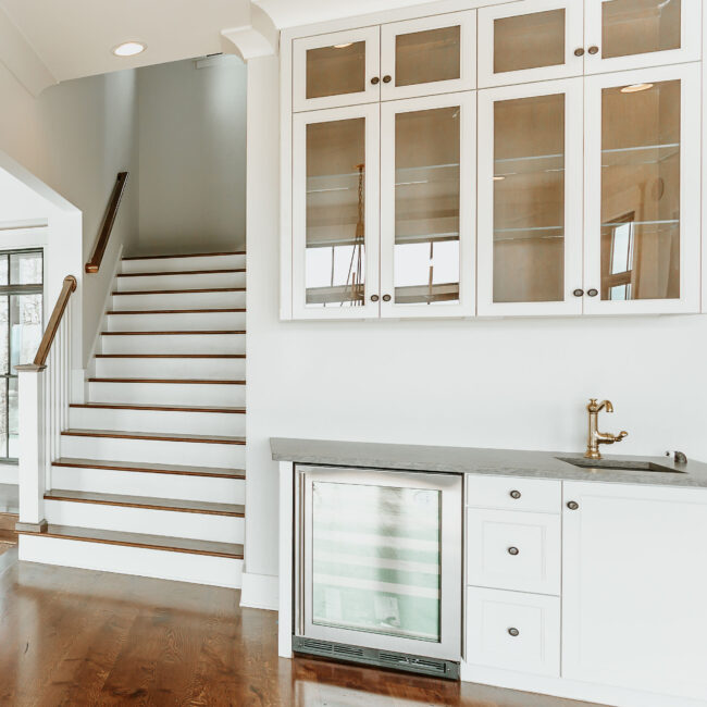 Staircase beside glass-front white cabinets and wine fridge in Mountain Vista by Mike Stevens Homes