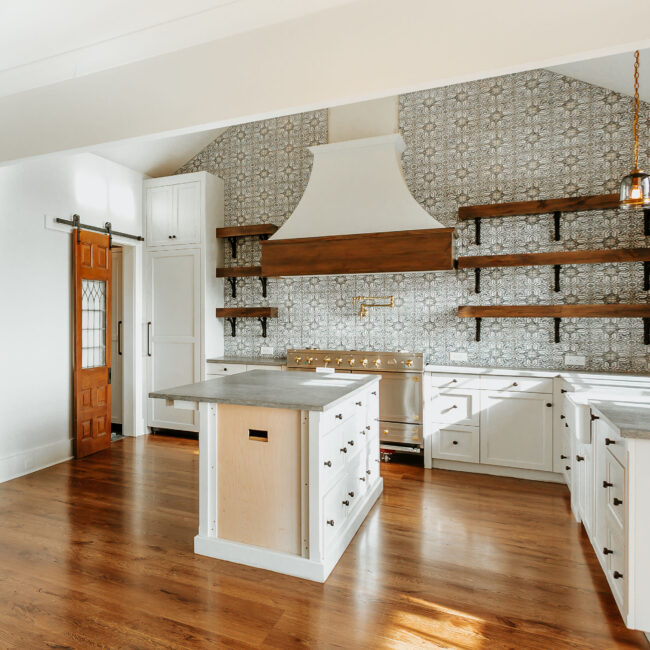 Kitchen with white cabinets, floating wood shelves and sliding barn door in Mountain Vista by Mike Stevens Homes