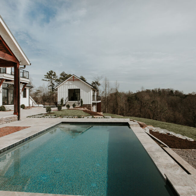 Rectangular pool with stone coping and white outbuilding beyond in Mountain Vista by Mike Stevens Homes