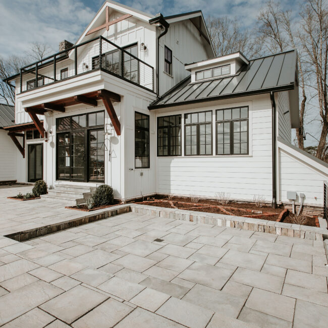 Flagstone patio behind white home with black-framed doors and dark metal roof in Mountain Vista by Mike Stevens Homes