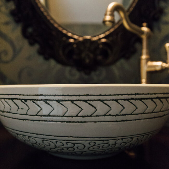 Vessel sink with patterned bowl and antique brass faucet in Haunted Mansion Homage, a custom home by Mike Stevens Homes