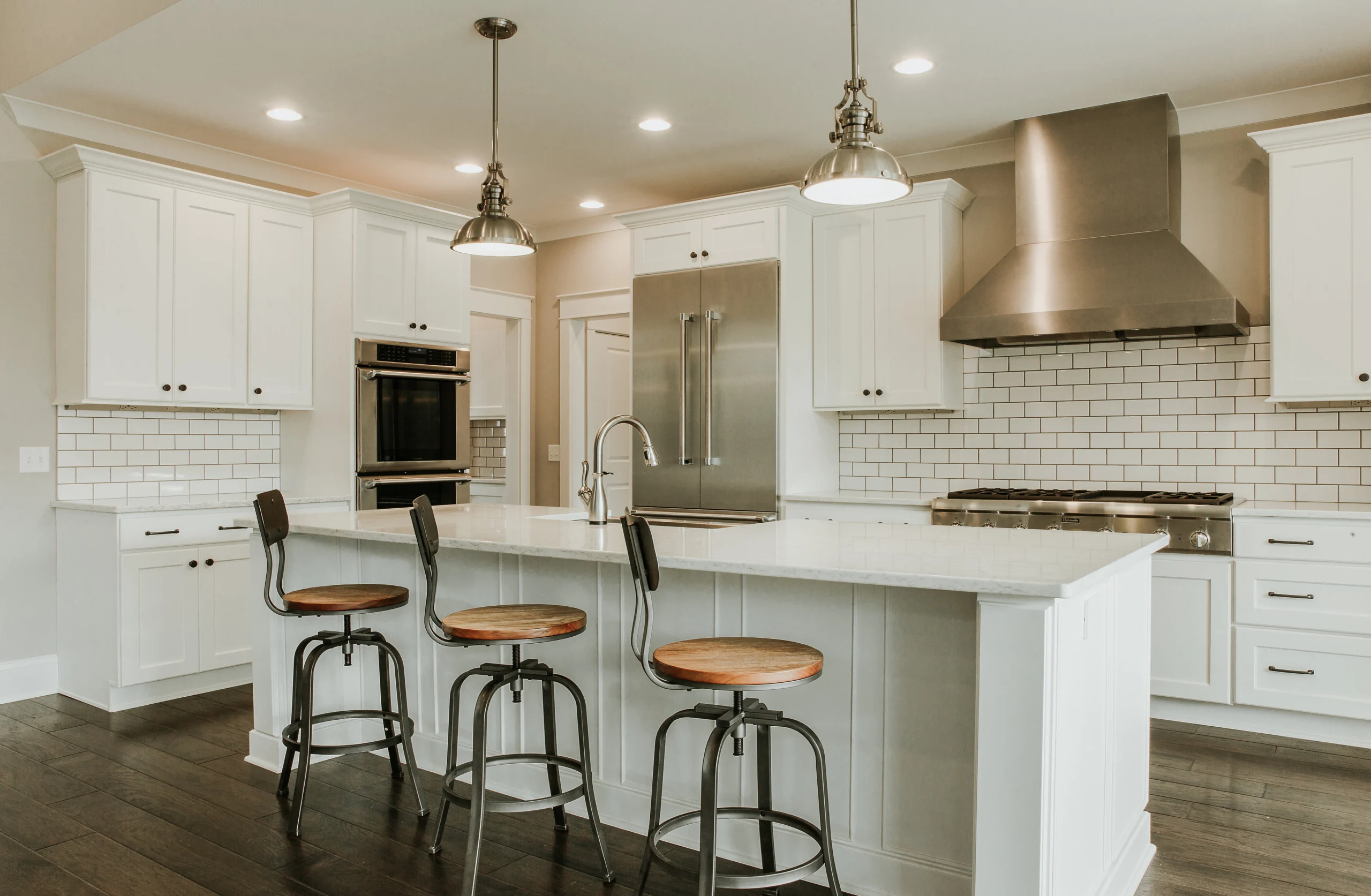 White kitchen with subway tile backsplash, pendant lights and island with barstools, by Mike Stevens Homes