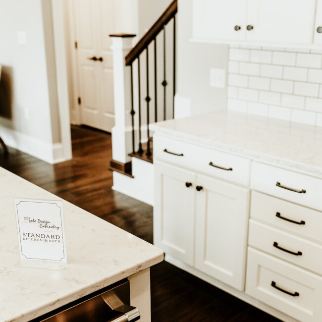 Kitchen island beside staircase with white cabinetry in Timeless Charm, a custom home by Mike Stevens Homes