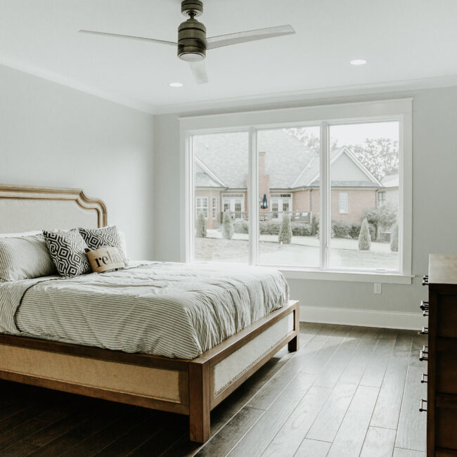 Primary bedroom with upholstered bed and front window in Timeless Charm, a custom home by Mike Stevens Homes