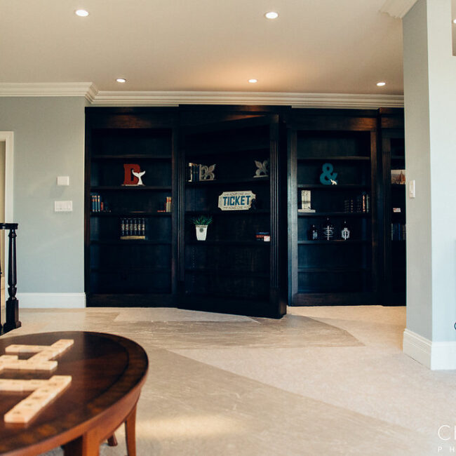 Dark built-in shelving wall in a room with round wood table in Haunted Mansion Homage, a custom home by Mike Stevens Homes