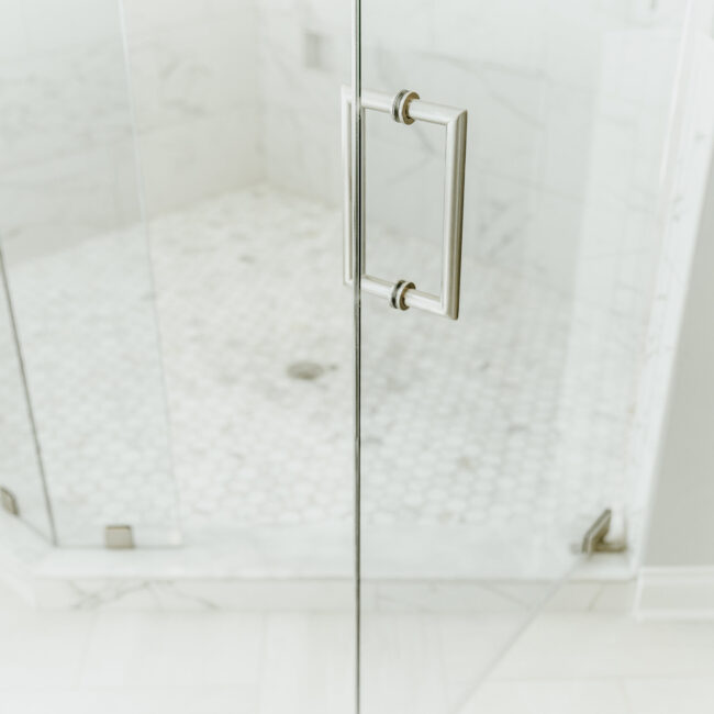 Glass shower door with hexagon floor tile in Timeless Charm, a custom home by Mike Stevens Homes