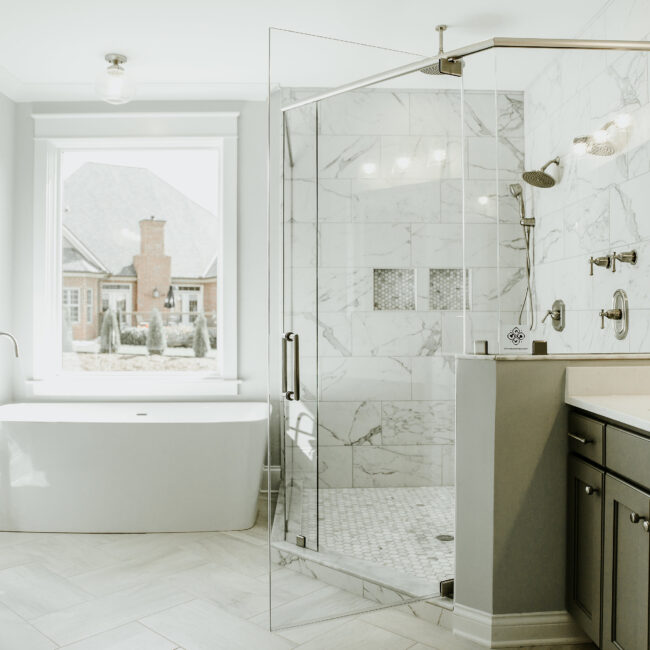 Glass shower beside freestanding tub at window in Timeless Charm, a custom home by Mike Stevens Homes