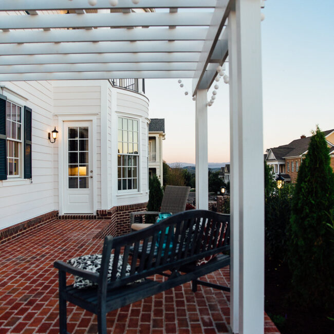 Brick patio with wood bench under white pergola in Haunted Mansion Homage, a custom home by Mike Stevens Homes