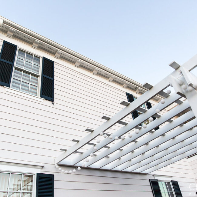 Close-up of white siding, black shutters and pergola beams in Haunted Mansion Homage, a custom home by Mike Stevens Homes
