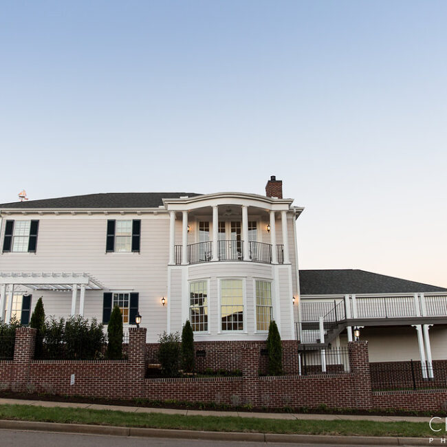 White home with columned balcony and brick base at dusk in Haunted Mansion Homage, a custom home by Mike Stevens Homes