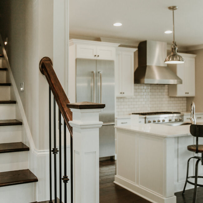 Wood staircase beside white kitchen with range hood in Timeless Charm, a custom home by Mike Stevens Homes