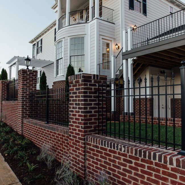 Brick wall and black iron fence beside a white porch in Haunted Mansion Homage, a custom home by Mike Stevens Homes