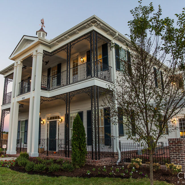 White two-story home with columns, iron balconies and garden in Haunted Mansion Homage, a custom home by Mike Stevens Homes