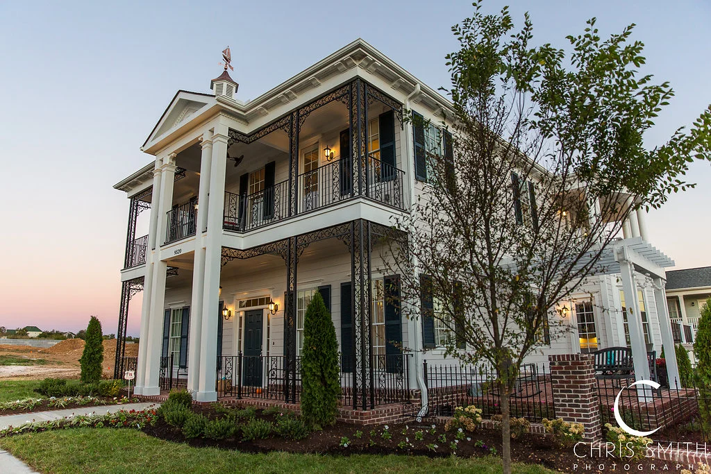 White two-story home with columns, iron balconies and garden in Haunted Mansion Homage, a custom home by Mike Stevens Homes