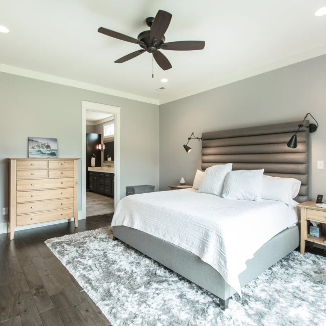 Primary bedroom with dark upholstered headboard and white bedding in Urban Farmhouse, a custom home by Mike Stevens Homes