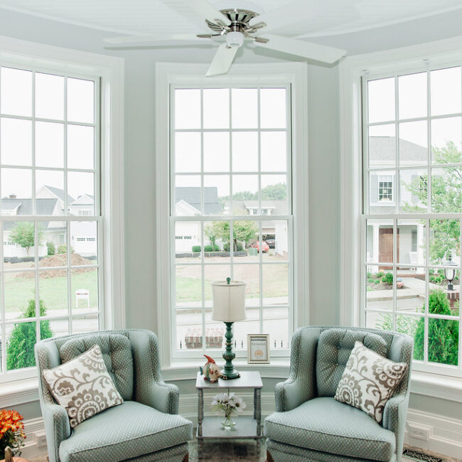 Sunroom with bay windows and blue-gray wingback chairs in Haunted Mansion Homage, a custom home by Mike Stevens Homes