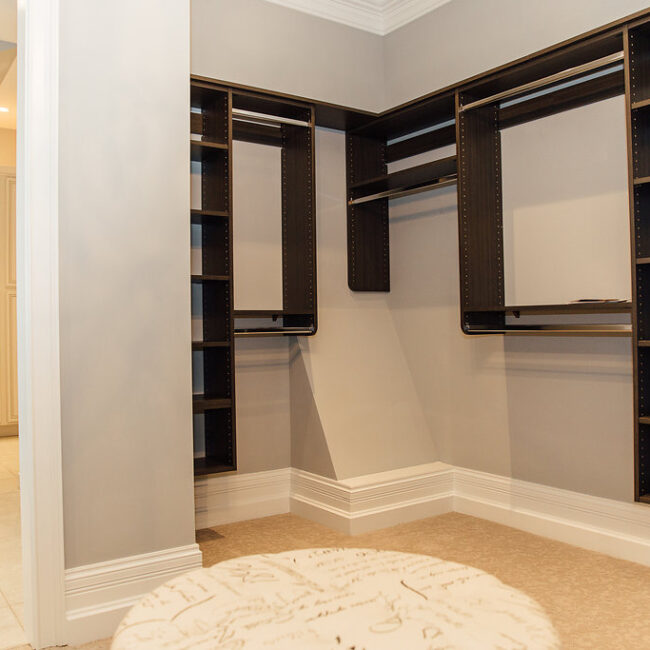 Walk-in closet with dark wood shelving and ottoman in Haunted Mansion Homage, a custom home by Mike Stevens Homes