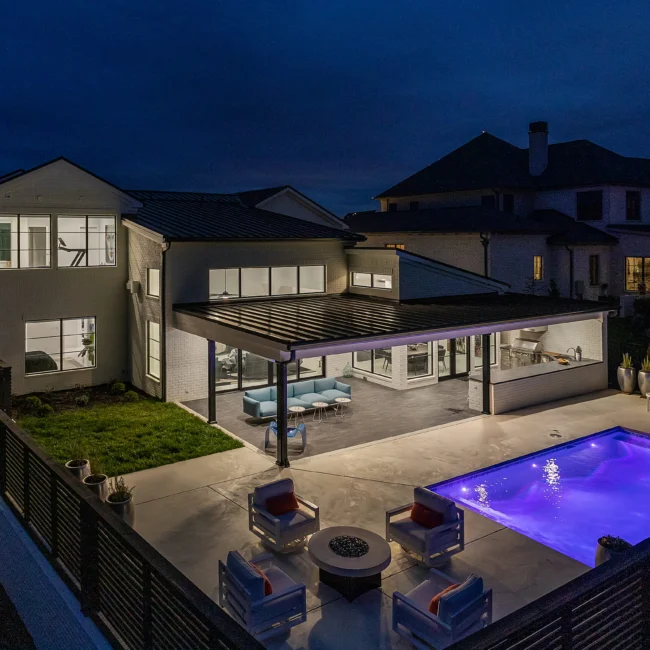 Backyard at dusk with pergola, lounge seating and illuminated pool in Urban Oasis by Mike Stevens Homes