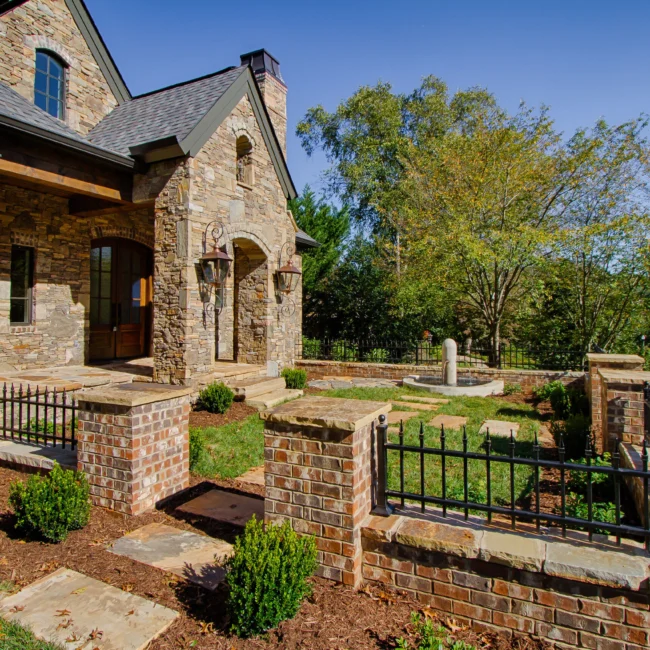Stone home front with brick wall, iron fence and stepping stone walk in European Villa, a custom home by Mike Stevens Homes