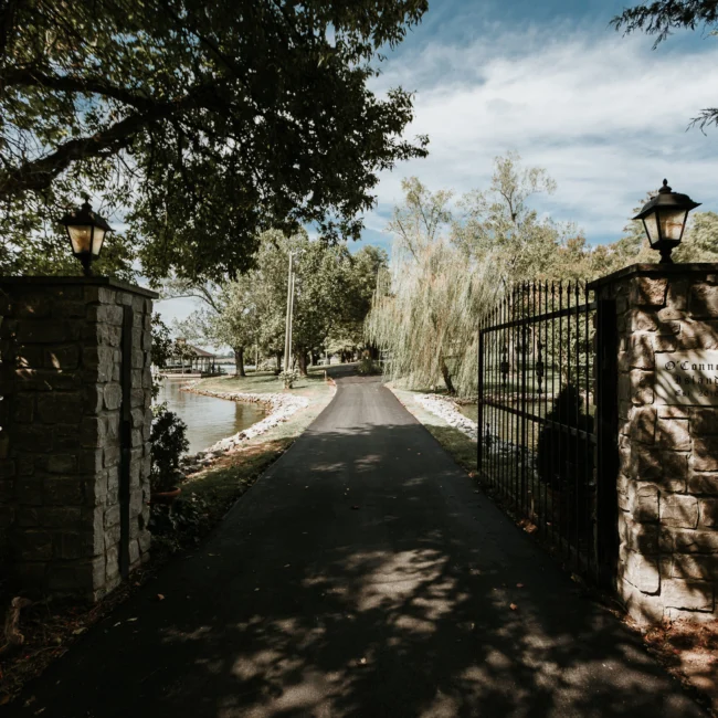 Long driveway through iron gate and stone pillars in Island Farmhouse, a custom home by Mike Stevens Homes
