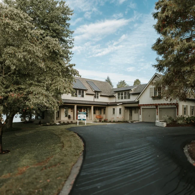 Front exterior with sweeping driveway and mature trees in Island Farmhouse, a custom home by Mike Stevens Homes
