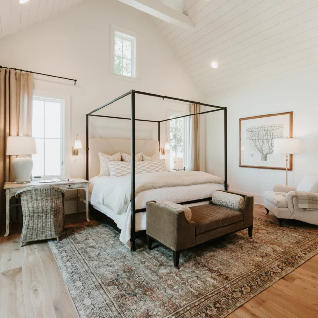 Primary bedroom with black canopy bed and patterned rug in Island Farmhouse, a custom home by Mike Stevens Homes