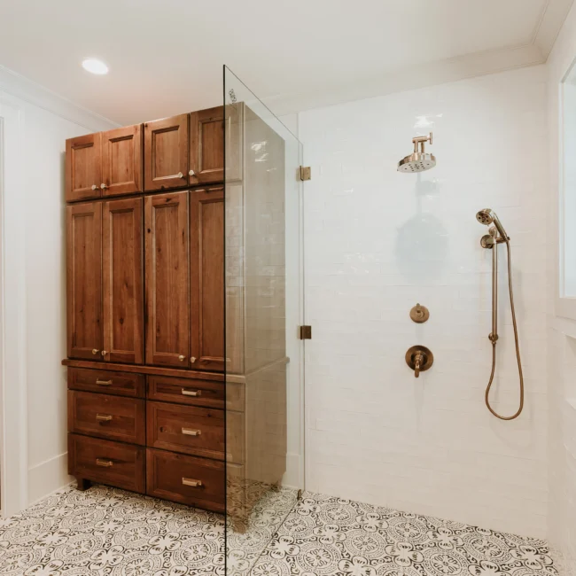 Shower with white tile and tall walnut linen cabinet in Island Farmhouse, a custom home by Mike Stevens Homes