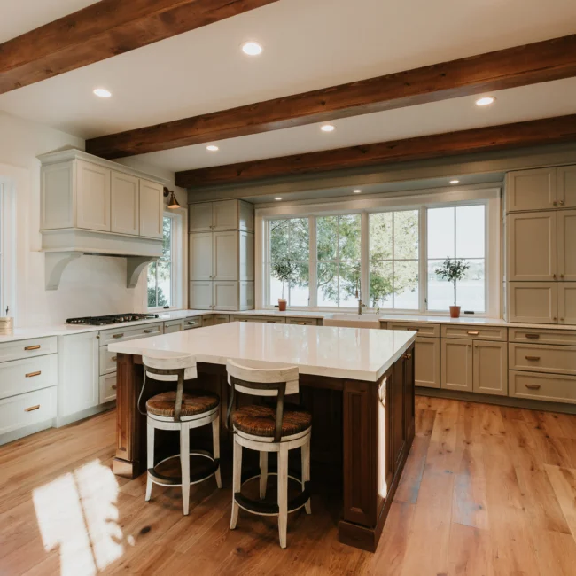 Kitchen with wood island, cream cabinets, and beams in Island Farmhouse, a custom home by Mike Stevens Homes