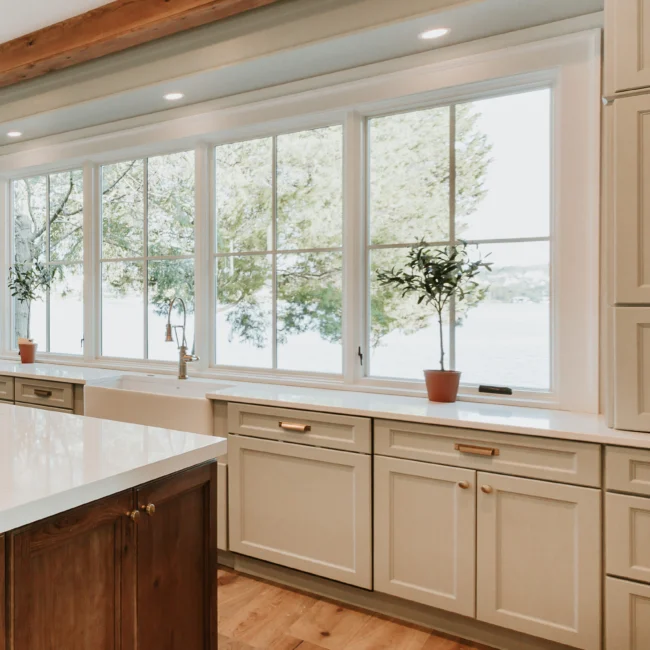 Kitchen with cream cabinets beneath tall windows in Island Farmhouse, a custom home by Mike Stevens Homes