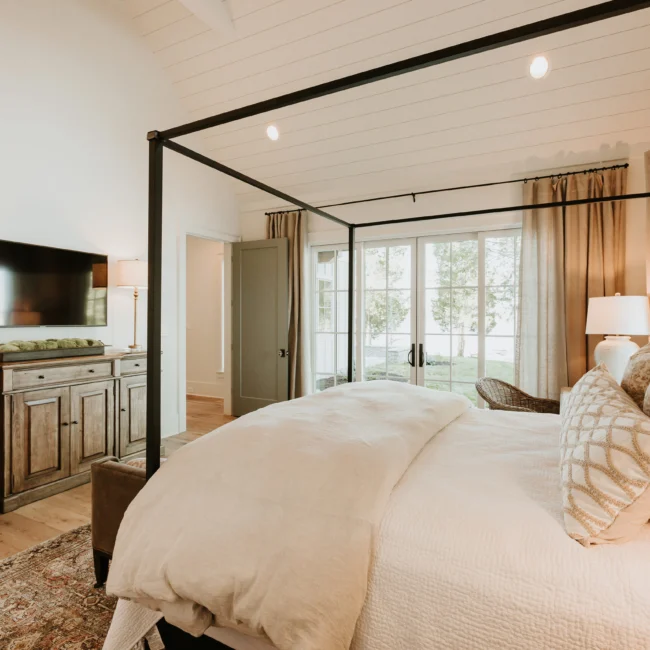 Primary bedroom with canopy bed and built-in media cabinet in Island Farmhouse, a custom home by Mike Stevens Homes