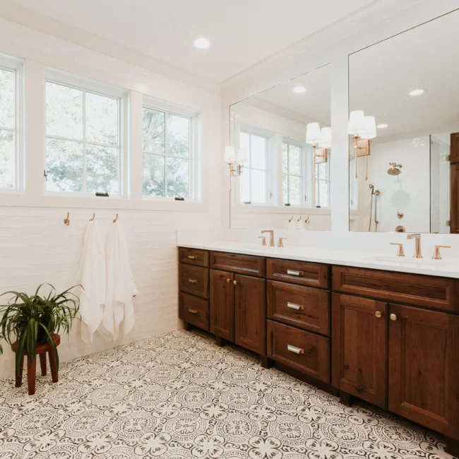 Primary bath with dark wood double vanity and patterned floor in Island Farmhouse, a custom home by Mike Stevens Homes