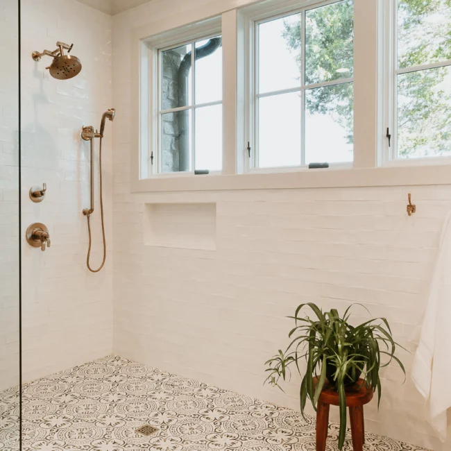 Glass shower with patterned floor tile and handheld showerhead in Island Farmhouse, a custom home by Mike Stevens Homes
