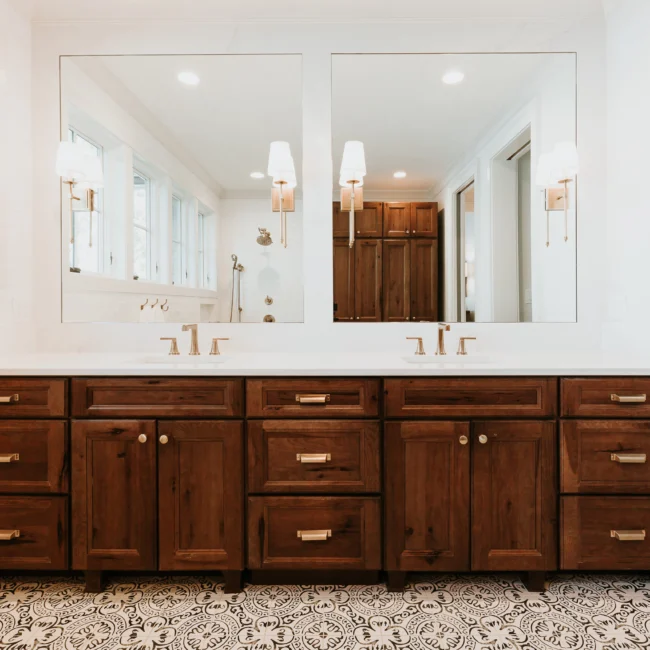 Primary bath with walnut double vanity and wall sconces in Island Farmhouse, a custom home by Mike Stevens Homes