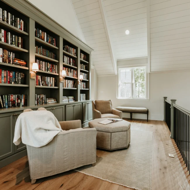 Library with built-in bookcases and reading chairs in Island Farmhouse, a custom home by Mike Stevens Homes