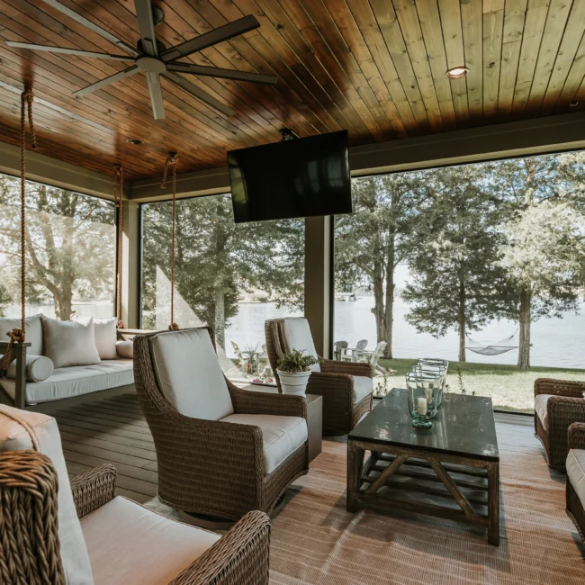 Screened porch with wood ceiling and wicker lounge chairs in Island Farmhouse, a custom home by Mike Stevens Homes