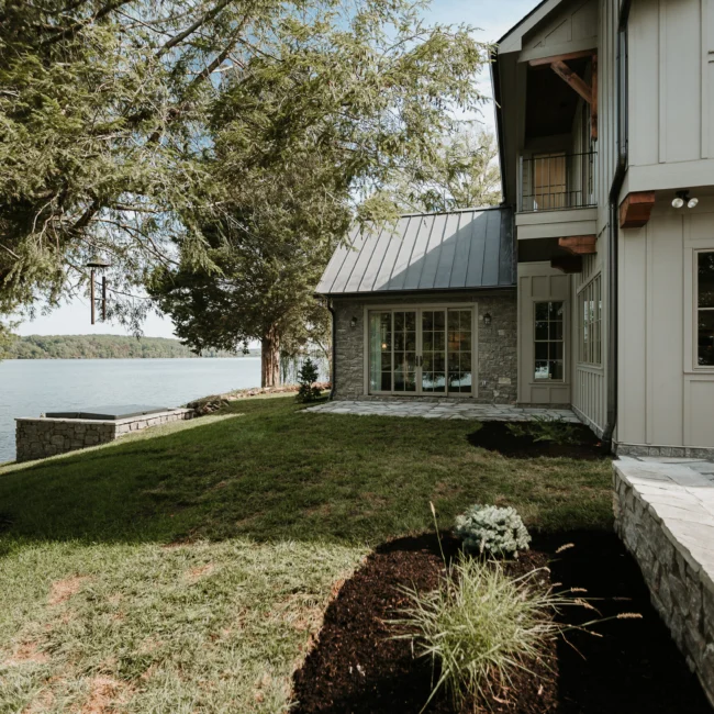 Backyard with stone and board-and-batten facade and lawn in Island Farmhouse, a custom home by Mike Stevens Homes