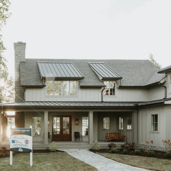 Front exterior with covered porch and metal-roof dormers in Island Farmhouse, a custom home by Mike Stevens Homes