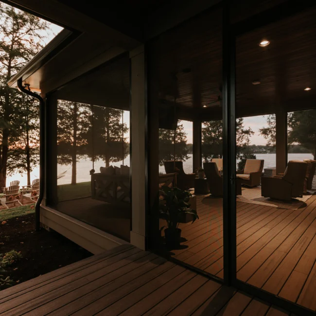 Screened porch at dusk with dark wood ceiling in Island Farmhouse, a custom home by Mike Stevens Homes