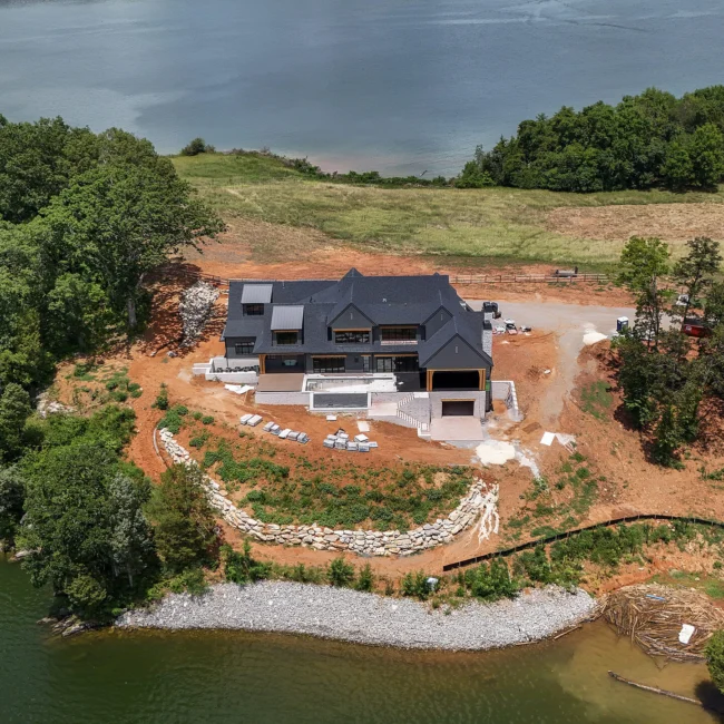 Aerial of home under construction on lakeside slope with rock walls in Edgewater Estate, a custom home by Mike Stevens Homes