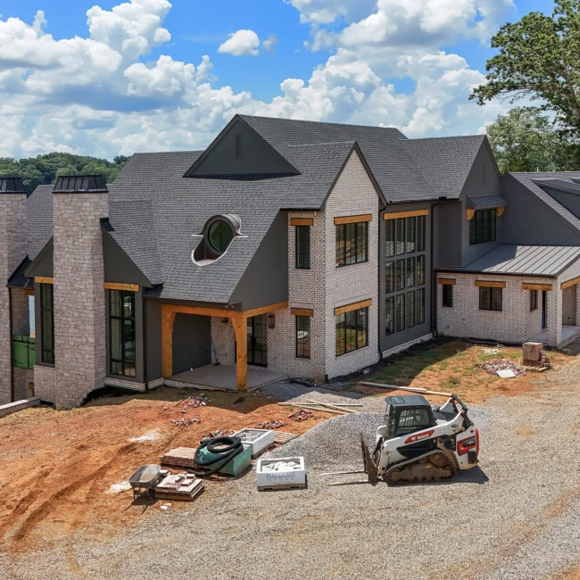Aerial of gray gabled home with timber accents on site in Edgewater Estate, a custom home by Mike Stevens Homes