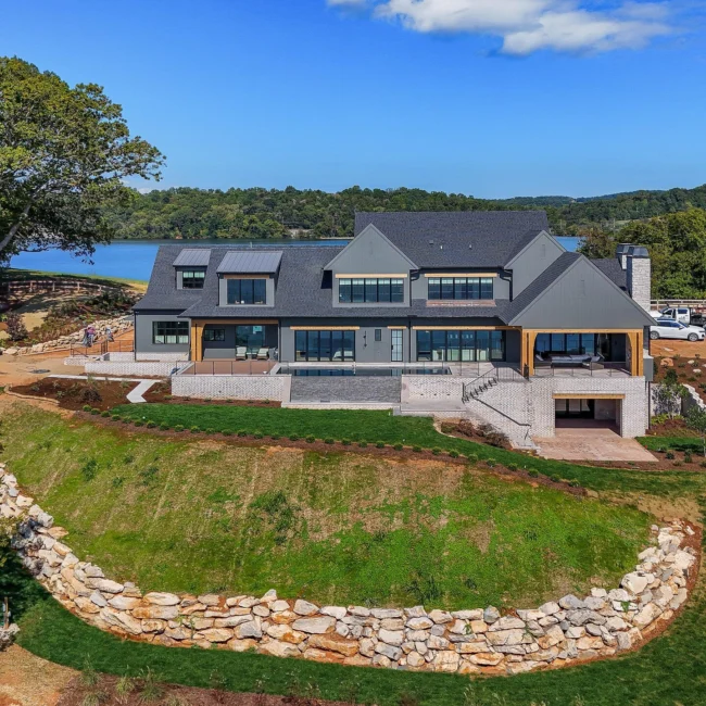 Aerial of lakefront home on grassy slope with stone retaining wall in Edgewater Estate, a custom home by Mike Stevens Homes