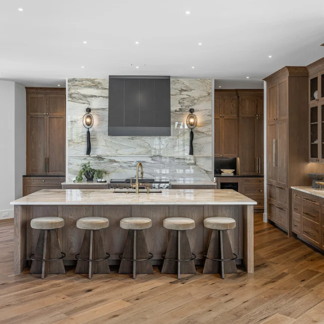Kitchen with marble-backed island, bar stools and wood cabinetry in The Sanctuary, a custom home by Mike Stevens Homes