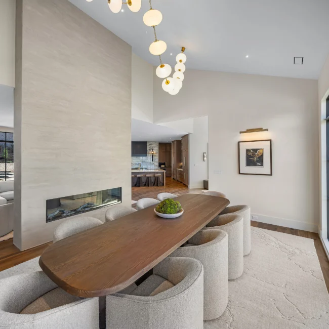 Dining room with oval wood table and curved chairs beside linear fireplace in The Sanctuary by Mike Stevens Homes
