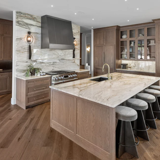 Kitchen with waterfall marble island, range hood and walnut cabinets in The Sanctuary by Mike Stevens Homes