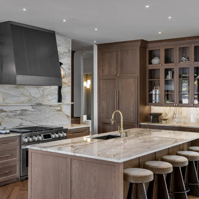 Kitchen with marble backsplash, gold faucet and stools at island in The Sanctuary, a custom home by Mike Stevens Homes